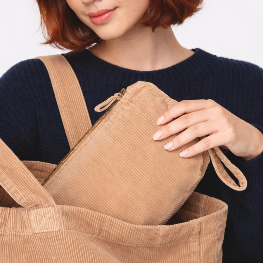 Beige toiletry bag with strap and zipper being pulled out of a tote bag.