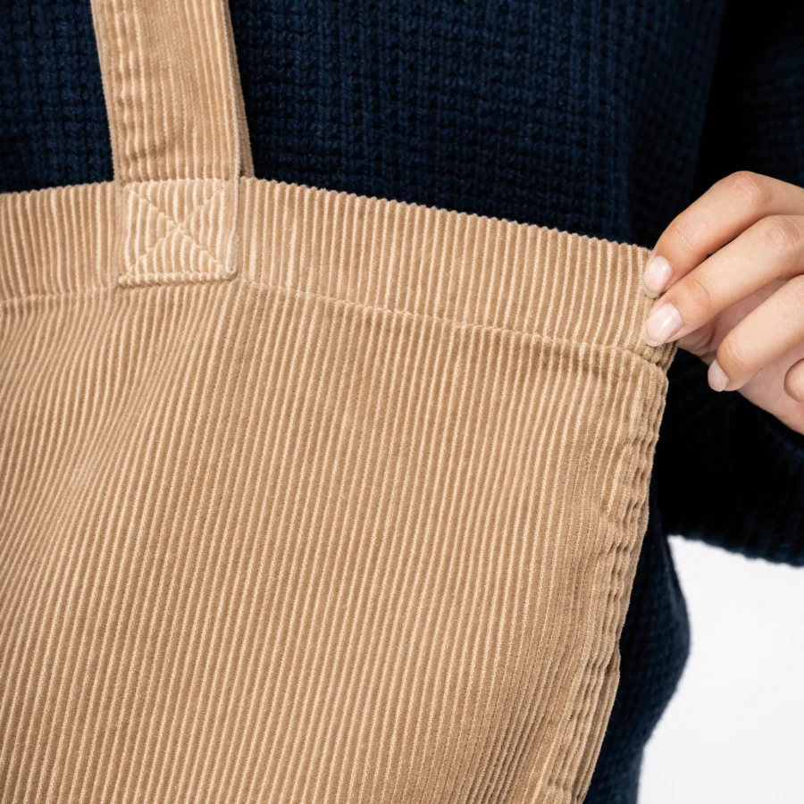 Brown bombazine bag with straps and stitching detail, being held by a hand.
