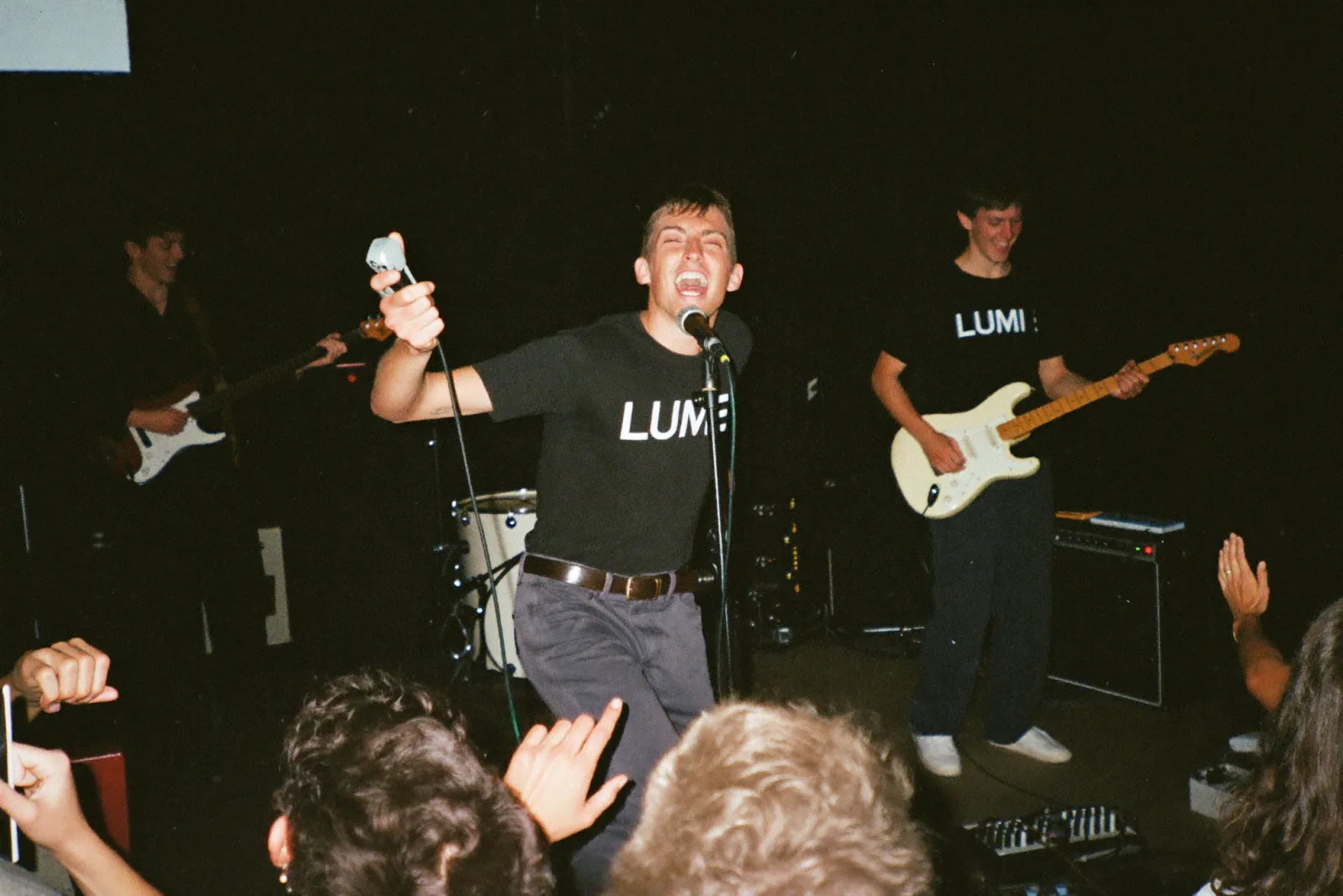 Banda em palco, todos com t-shirts pretas iguais estampadas com o nome da banda